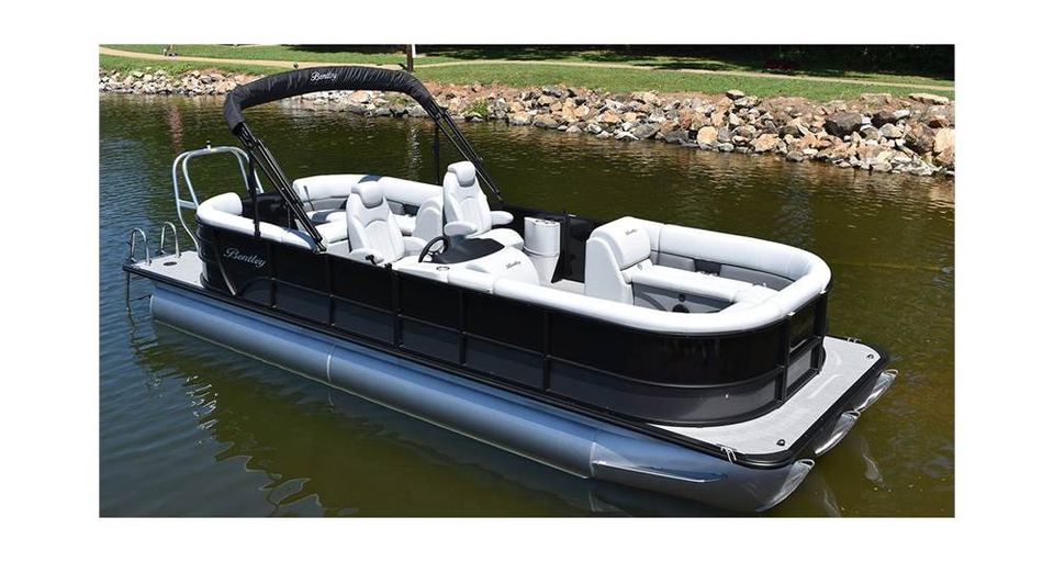 Black and white Bentley Navigator 243 tritoon on the water near a rocky shoreline
