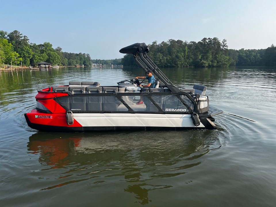 Red and white Sea-Doo Switch tritoon on calm water near a tree-lined shore